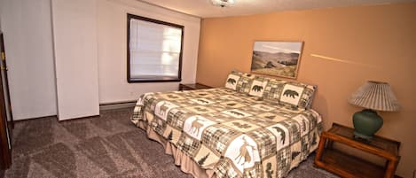 A bedroom with a large bed, a window with blinds, a lamp on a side table, and a ceiling light.