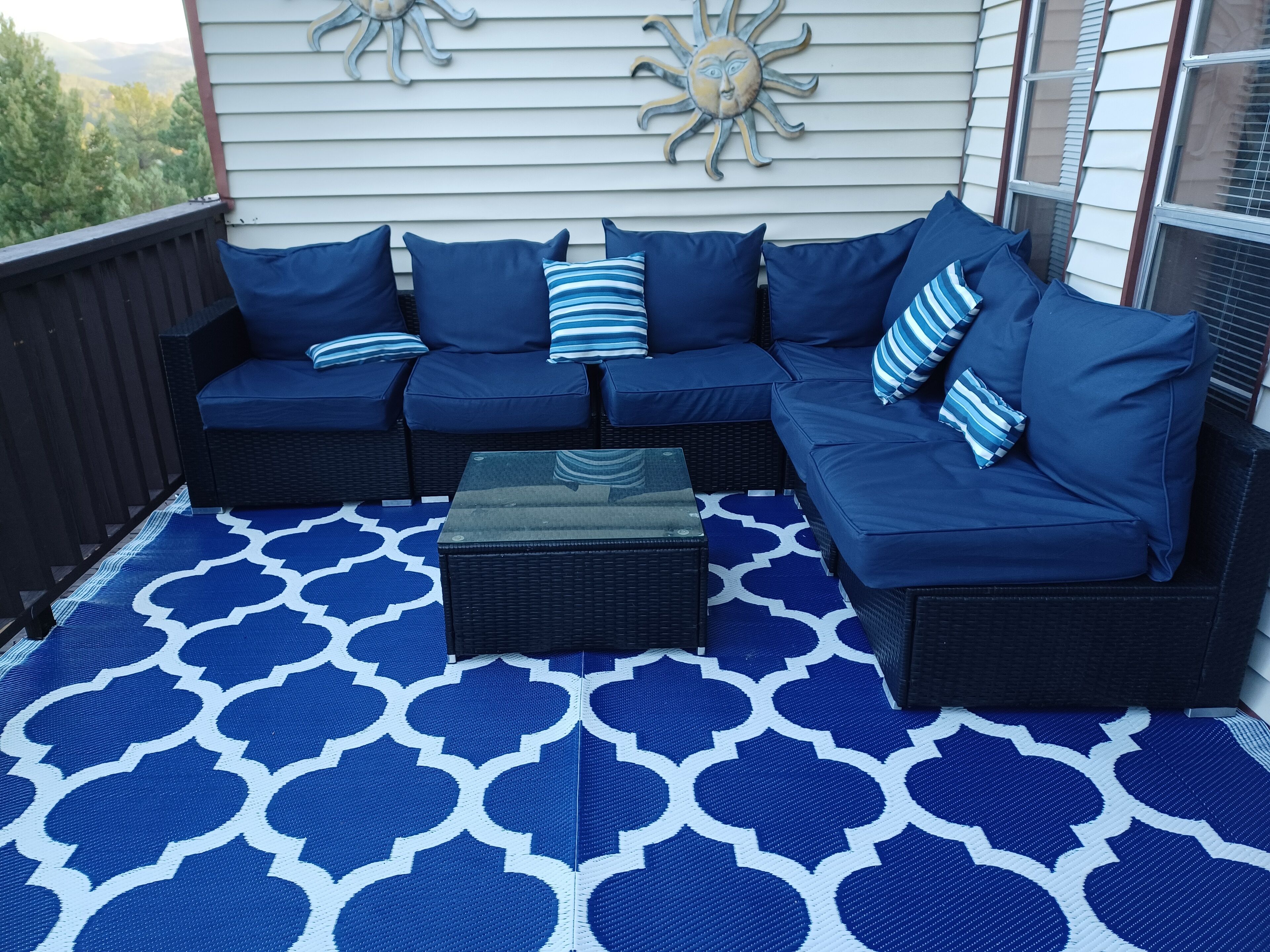 Een modulaire bank met blauwe kussens en een vloerkleed met patroon op een balkon.