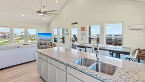 A spacious kitchen with a large island, granite countertops, and a view of the beach. - The Shore House 3 Bedroom Home by RedAwning (Port Bolivar)
