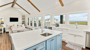 Una cocina amplia con una isla grande, armarios blancos y vista al océano.