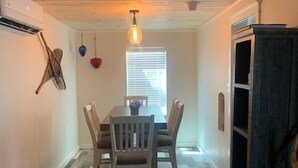 A dining area with a wooden table and chairs, a hanging light fixture, and a window with blinds.
