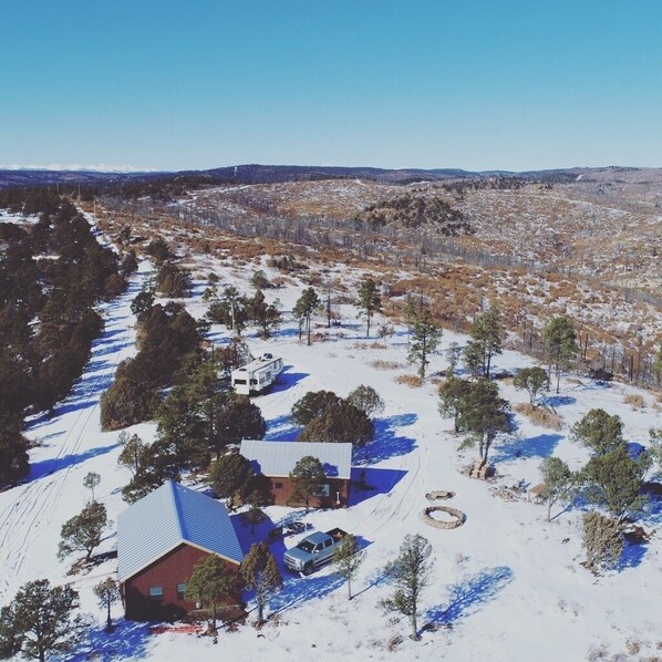 A house with a blue roof and a red brick section, surrounded by snow-covered ground and sparse trees.