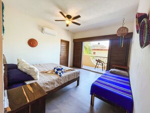 A room with a bed, a sofa, a ceiling fan, an air conditioning unit, and a view of the outside.