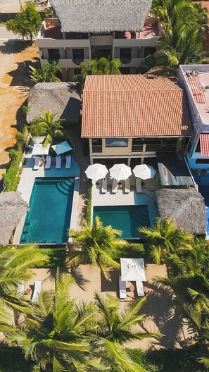 A resort with a swimming pool, lounge chairs, and thatched-roof structures.