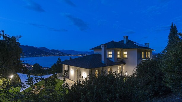 A two-story house with a large balcony, surrounded by greenery and overlooking a body of water. - Wonderful private villa with hot tub, sauna, private pool, WIFI, A/C, TV, patio and panoramic view (Baveno)