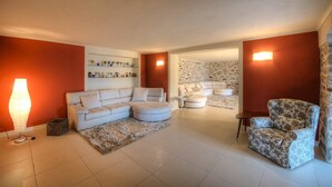 A living room with a sofa, ottoman, and armchair, a rug, and a wall with decorative items. - Wonderful private villa with hot tub, sauna, private pool, WIFI, A/C, TV, patio and panoramic view (Baveno)
