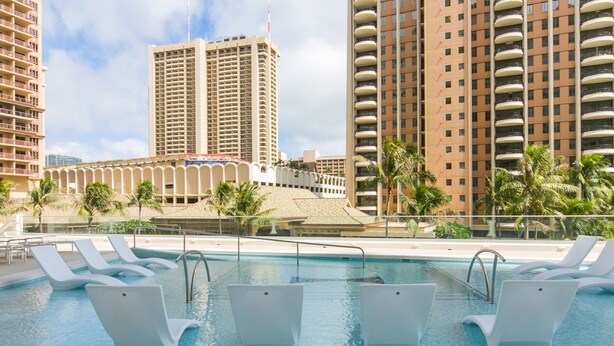 A swimming pool with white lounge chairs, surrounded by palm trees and tall buildings. - Ilikai Tower 1113 - Fully furnished condo with free wifi by RedAwning (Honolulu)