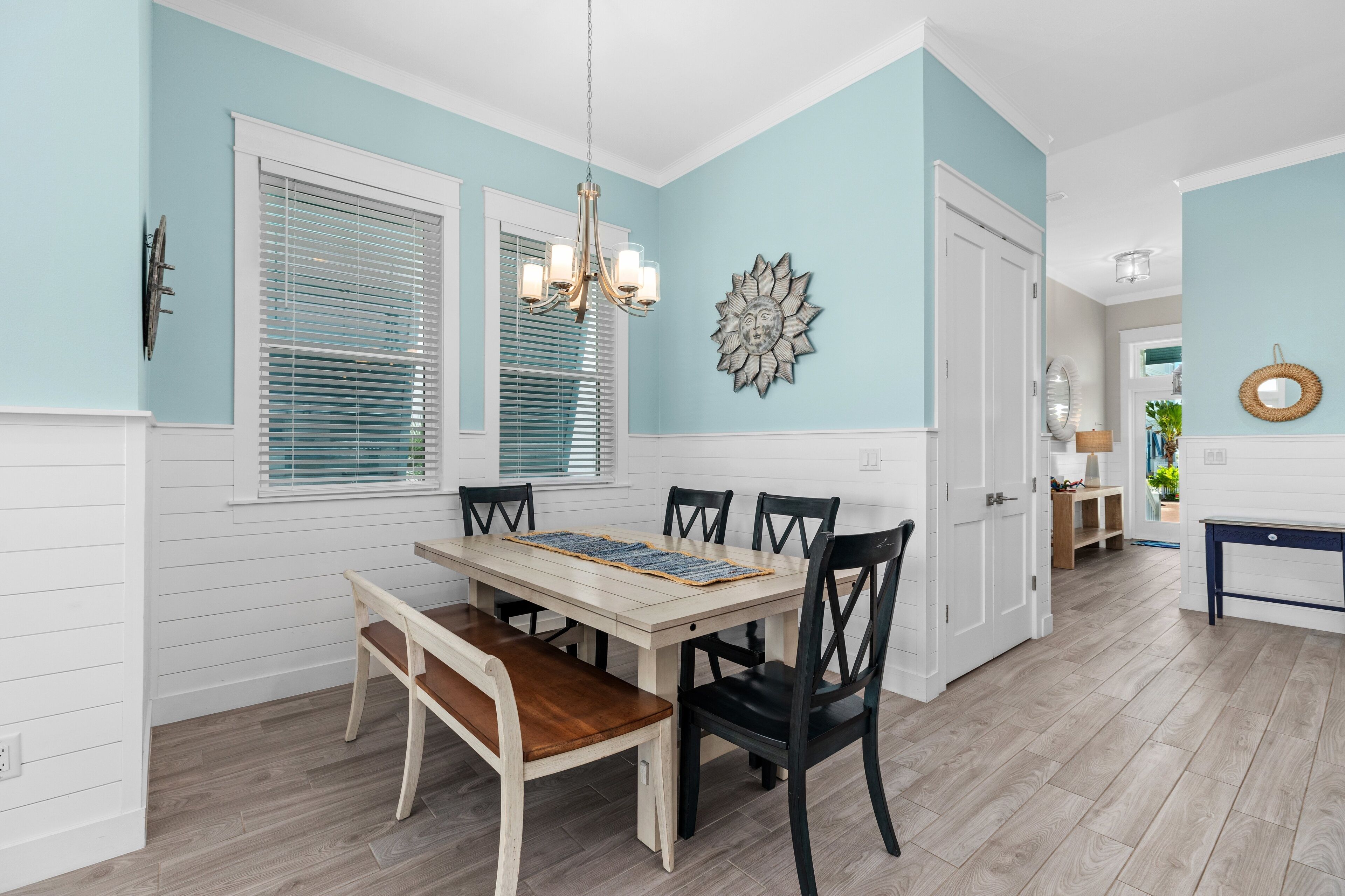 A dining room with a wooden table, four chairs, a bench, and a chandelier.