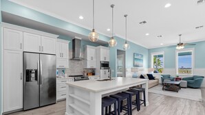Cocina moderna con armarios blancos, un refrigerador de acero inoxidable y una isla central con taburetes de bar.