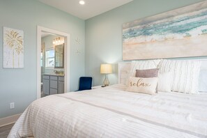 A bedroom with a bed, a nightstand, a lamp, a painting, and a view of the bathroom. - 1 Naut On Call 3 Bedroom Home by RedAwning (Port Bolivar)