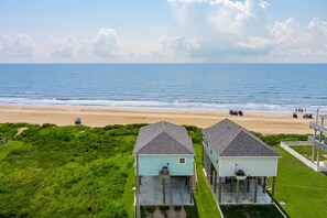 A beachfront property with two light blue houses, a sandy beach, and the ocean in the background. - 1 Naut On Call 3 Bedroom Home by RedAwning (Port Bolivar)