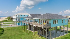 Ein direkt am Strand gelegenes Anwesen mit erhöhten Gebäudeteilen, einer überdachten Terrasse und Blick auf den Strand.