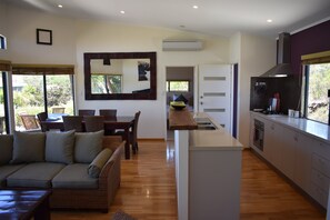 A modern kitchen with a central island, a dining area with a sofa and chairs, and a large mirror on the wall. - Good Ocean and National park View (Redgate)