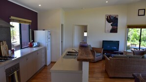 Una cocina moderna con una isla central, un comedor con mobiliario de mimbre y un televisor en la sala de estar.