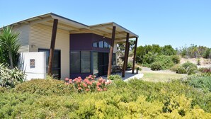 Una casa moderna con un porche cubierto, un pequeño jardín con flores rosadas y un cielo azul despejado.