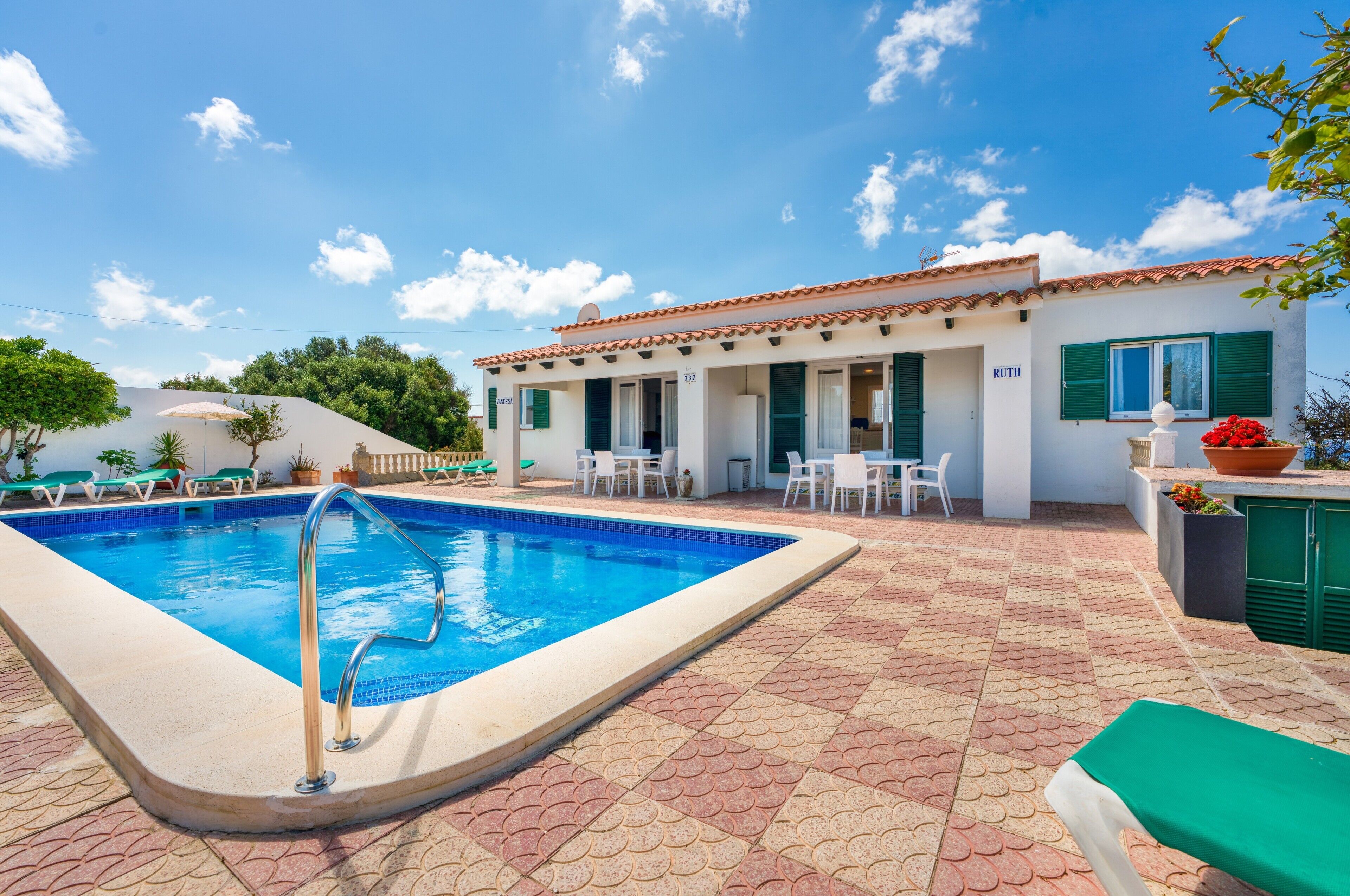 A swimming pool with a tiled deck, a building with a tiled roof, and outdoor seating.