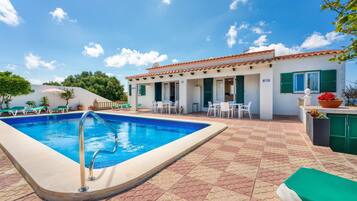 A swimming pool with a tiled deck, a building with a tiled roof, and outdoor seating.