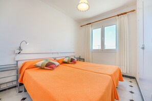 Una habitación con dos camas, una ventana con cortinas, un radiador y una lámpara.
