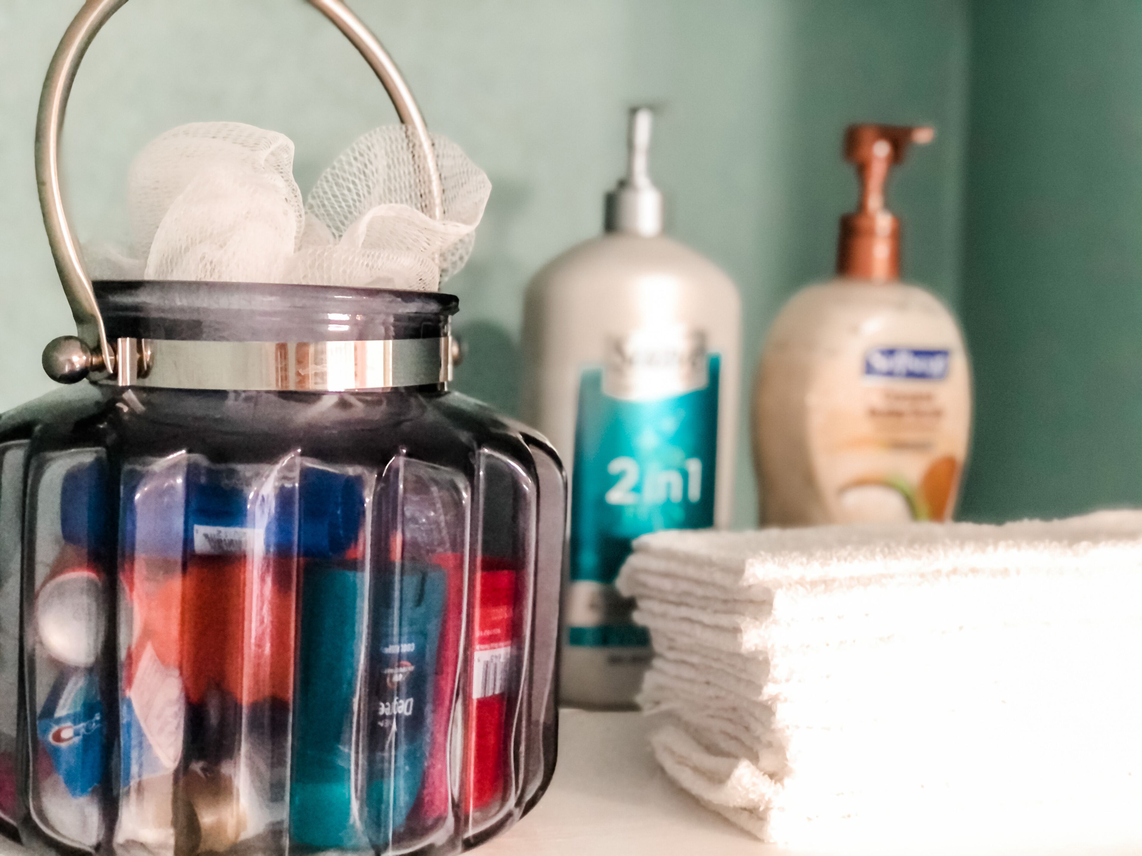 A bathroom with a glass container holding toiletries, a stack of white towels, and two bottles of lotion.