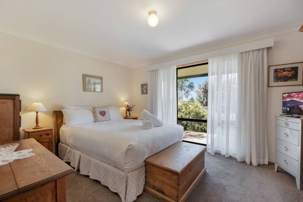 A bedroom with a large bed, a wooden bench, a dresser, and a window with curtains.