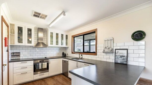 A modern kitchen with white cabinets, a stainless steel range hood, a built-in oven, and a large island with a dark countertop. - Ithaca Cottage by Your Innkeeper Mudgee (Frog Rock)