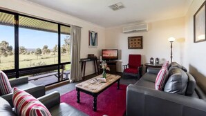 A spacious living room with a large window, a television, and a red armchair. - Ithaca Cottage by Your Innkeeper Mudgee (Frog Rock)