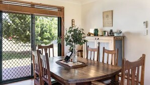 A dining area with a wooden table, chairs, a potted plant, and a kitchen area in the background. - Ithaca Cottage by Your Innkeeper Mudgee (Frog Rock)