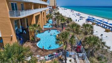 Um hotel com piscina, rodeado por palmeiras e uma praia.