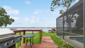 Una terraza de madera con una parrilla, una mesa y sillas con vista a un lago.