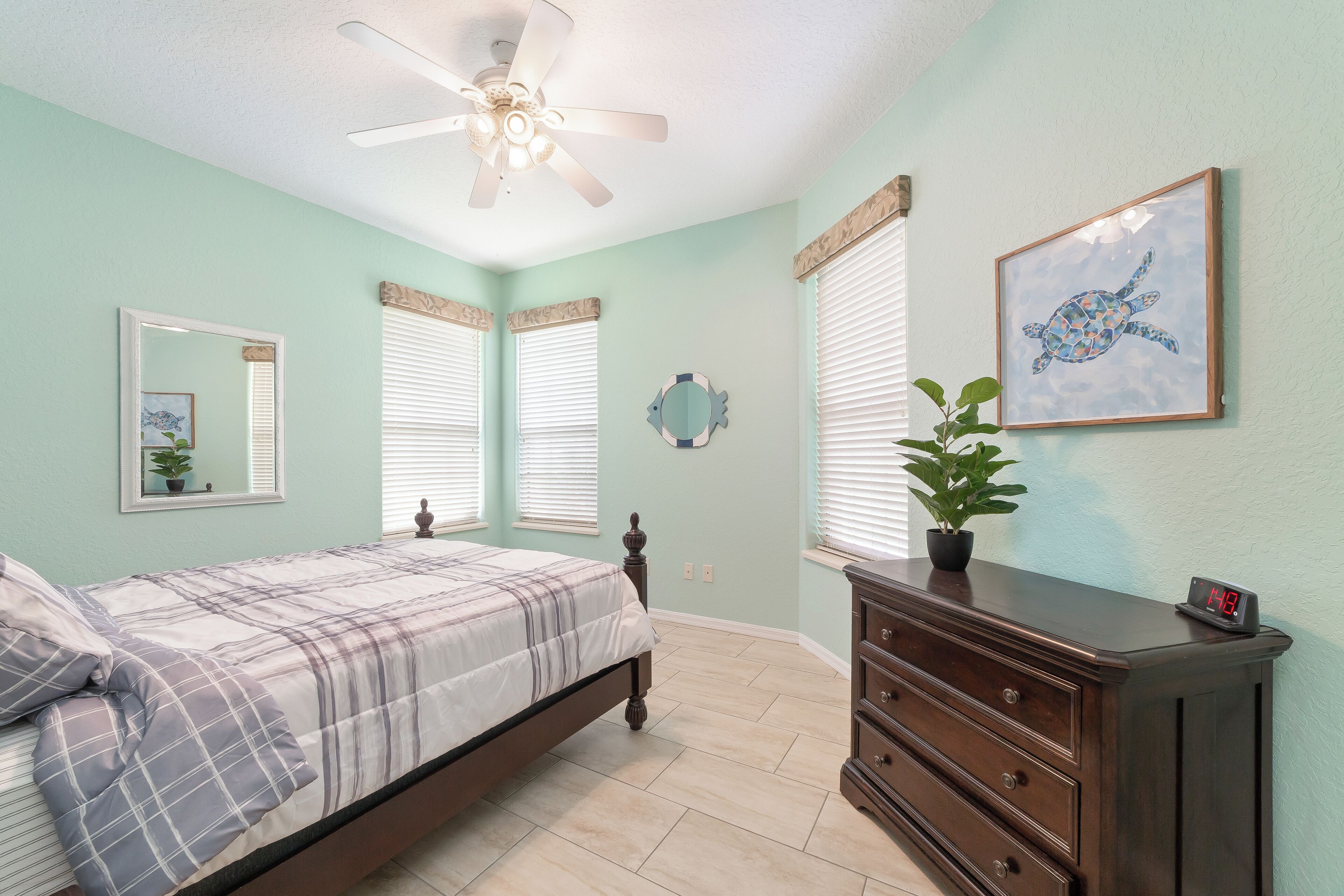 Une chambre à coucher comprenant un lit, une commode, un ventilateur de plafond et un tableau encadré accroché au mur.