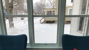 Two blue armchairs facing a window with a view of a snowy yard and a house. - Cottage Just 2 Blocks to Beach and Town (East Tawas)