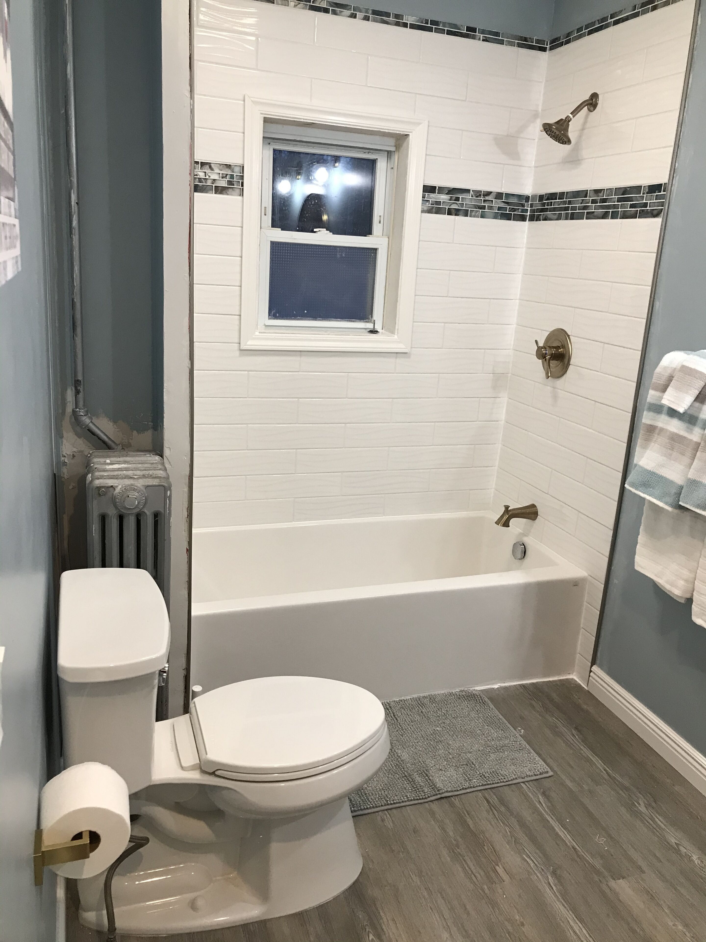 Une salle de bain avec une baignoire blanche, des toilettes et une fenêtre au-dessus du lavabo.