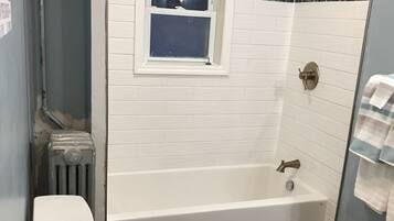 Une salle de bain avec une baignoire blanche, des toilettes et une fenêtre au-dessus du lavabo.