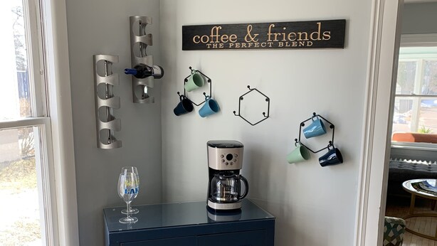 A corner room with a dark blue cabinet, a coffee maker, and wall-mounted hooks with mugs. - Cottage Just 2 Blocks to Beach and Town (East Tawas)