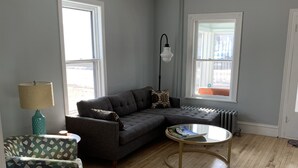 A living room with a sectional sofa, a round coffee table, and a patterned armchair. - Cottage Just 2 Blocks to Beach and Town (East Tawas)