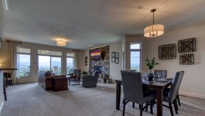 A spacious living area with a fireplace, a dining table set for four, and a large window offering a view of the mountains. - Panoramic Mountain Range Views! Spacious 2 King BR Chalet w/Garage, Jacuzzi, WiFi & Free Tickets (Sevierville)