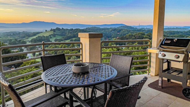 A balcony with a table and chairs, a grill, and a scenic view of hills and valleys. - Panoramic Mountain Range Views! Spacious 2 King BR Chalet w/Garage, Jacuzzi, WiFi & Free Tickets (Sevierville)