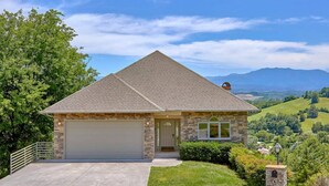 A single-story house with a stone facade, a garage, and a well-maintained lawn. - Panoramic Mountain Range Views! Spacious 2 King BR Chalet w/Garage, Jacuzzi, WiFi & Free Tickets (Sevierville)