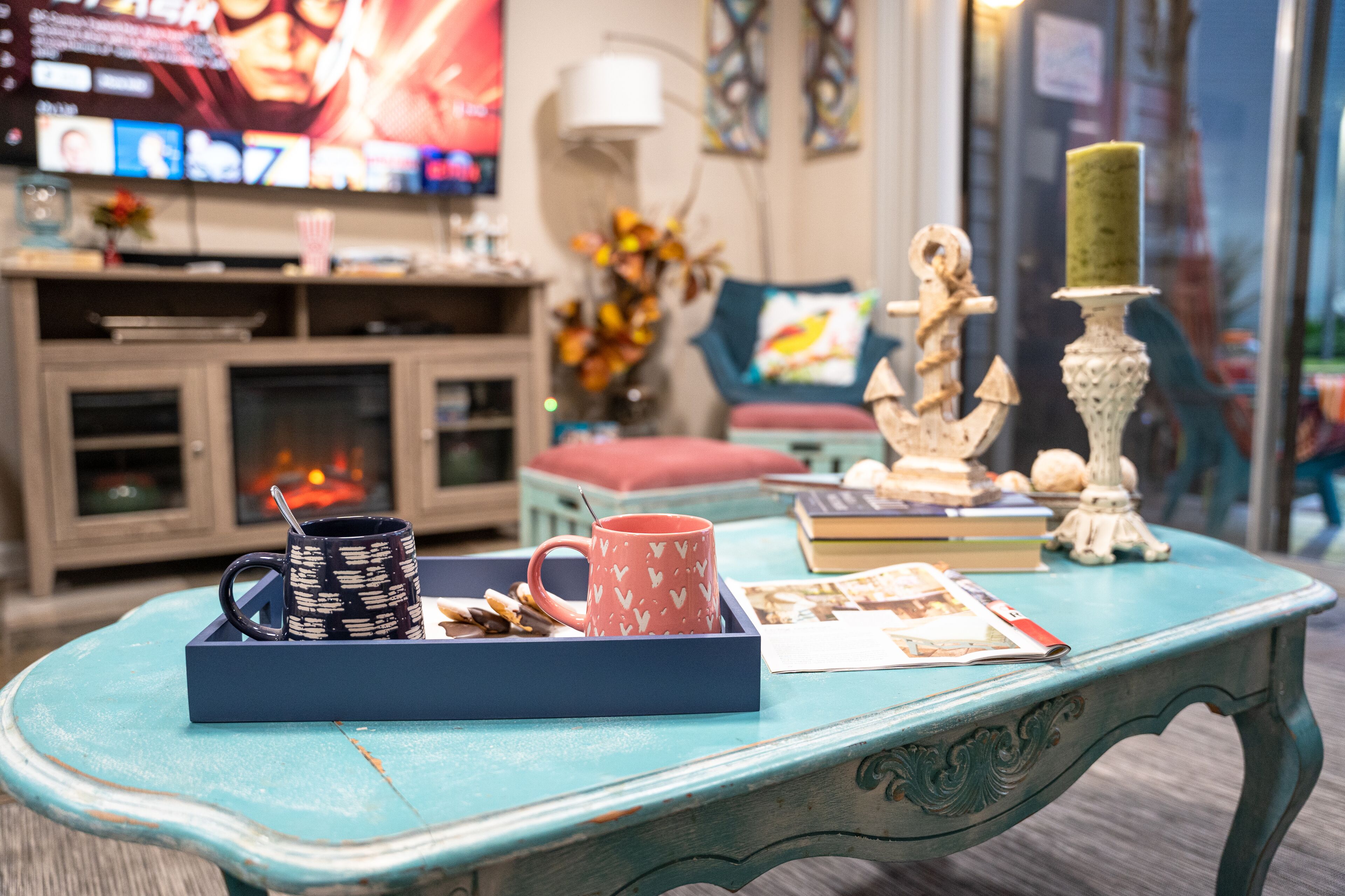 A cozy living room with a fireplace, a television, and a coffee table with a tray of snacks and a mug.