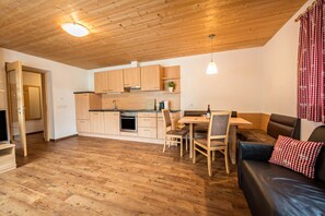 Une cuisine moderne avec des meubles en bois, un coin repas avec une table et des chaises, et un canapé en cuir agrémenté d’un coussin rouge.