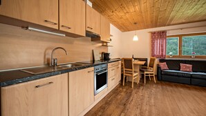 Una cocina moderna con armarios de madera, horno empotrado y comedor con sofá negro y cojines rojos.