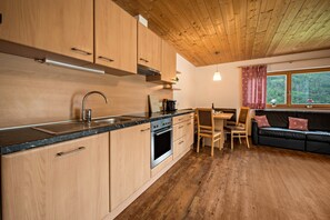 Une cuisine moderne avec des meubles en bois, un four encastré et un coin repas comprenant un canapé noir et des coussins rouges.