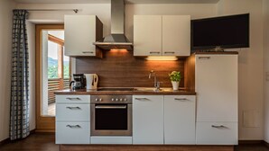 Una cocina moderna con armarios blancos, estufa de acero inoxidable, horno empotrado, pileta y televisor de pantalla plana montado sobre los armarios.