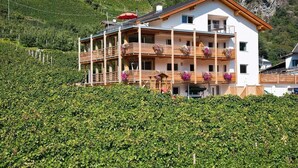 Un edificio de varios pisos con balcones, rodeado de vegetación exuberante y montañas al fondo.