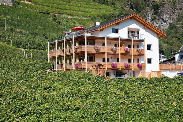 Un immeuble à plusieurs étages doté de balcons, entouré d’une végétation luxuriante et ayant une chaîne de montagnes en toile de fond.