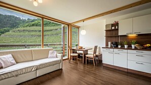 Una cuina moderna amb armaris de fusta, una zona de menjador amb taula i cadires, i una finestra gran amb vista a una vinya.
