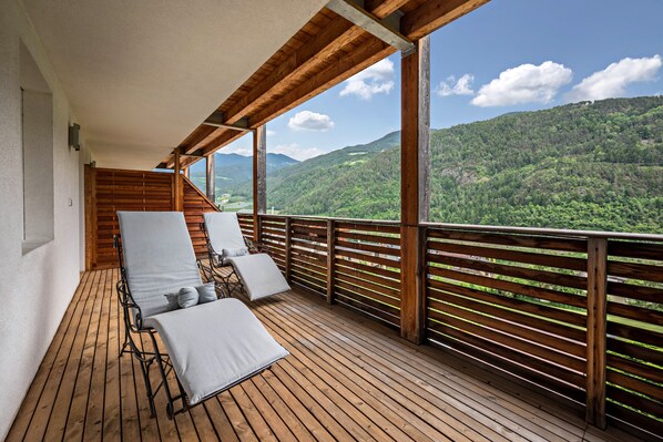 Terraza de madera con sillones de descanso y vista a un paisaje montañoso.