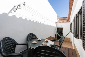 A patio with a table and chairs, a hammock, and a white building with a tiled roof.