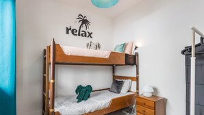 Una cama litera con estructura de madera, una mesita de noche con cajones, un estante en la pared y un letrero que dice 'relax' con una palmera.