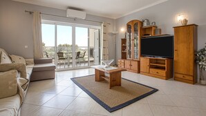 Un salon avec un canapé, un téléviseur, un meuble en bois et une vue à travers la porte vitrée.